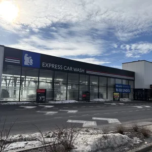 Express automazgātava ēka ar stiklotu fasādi saulainā dienā.