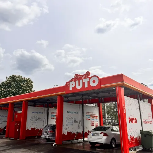 Automazgātava sarkanās un baltās krāsās zem mākoņainām debesīm.