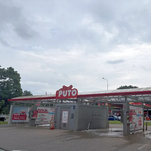 Auto mazgātava ar jumtu, sarkaniem akcentiem un mākoņainu debesu fona.