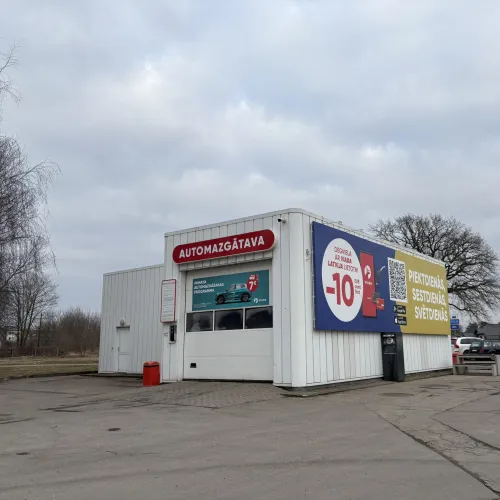 Automazgātava pelēkā dienā ar reklāmu uz sienas.