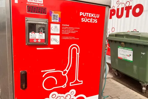 Sarkana putekļsūcēja automāts blakus zaļam konteineram.