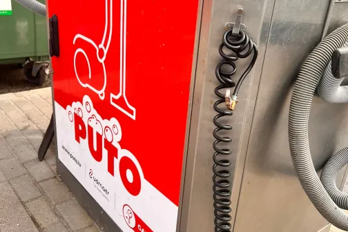 Metāla putekļusūcējs ar sarkanu reklāmas uzlīmi stāv uz ielas.