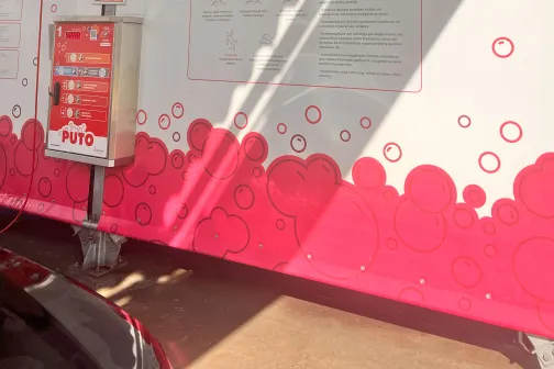 Auto mazgā&scaron;anas stacija ar sarkanu un baltu dizainu, attēlots auto ar putām.