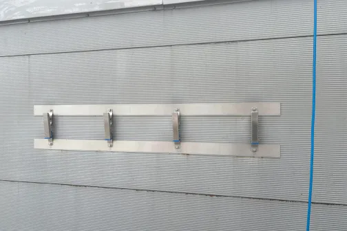 Metāla stiprinājumi uz pelēkas sienas ar zilu cauruli.