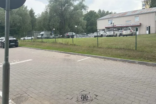 Autostāvvieta blakus ēkai ar automa&scaron;īnām un kokiem fona.