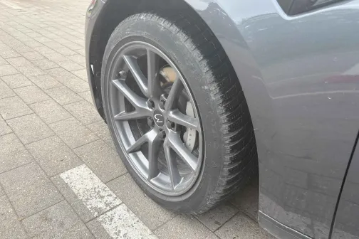 Pelēka auto priek&scaron;ējais ritenis stāvlaukumā.