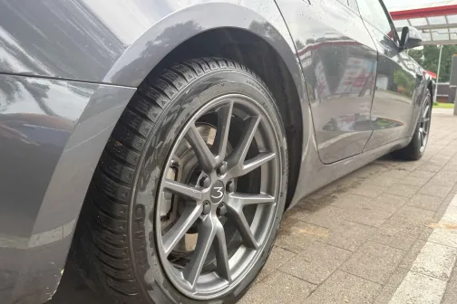 Pelēka auto labā aizmugurējā riepa uz mazgā&scaron;anas laukuma.