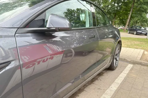 Pelēka automa&scaron;īna stāvvietā, tās virsmā redzams koku atspīdums.