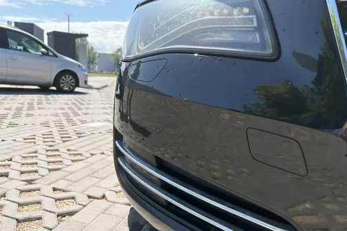 Spīdīgs melns auto buferis saulainā dienā, fonā sudrabaina automa&scaron;īna.