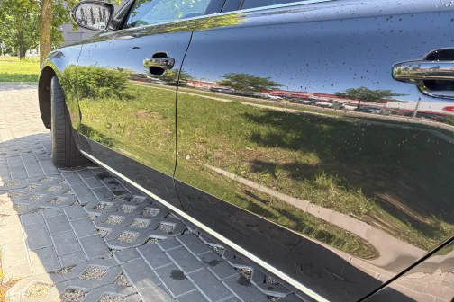 Melnas automa&scaron;īnas sānu durvis atspoguļo zaļu apkārtni saulainā dienā.