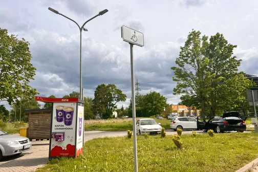 Stāvvietas zīme ar koku un ma&scaron;īnām fonā, mākoņaina diena.