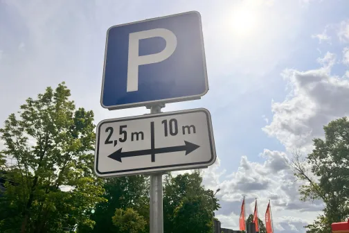 Stāvvietas zīme saulainā dienā ar kokiem fonā.