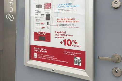 Reklāmas plakāts uz pelēkas sienas pie durvīm.