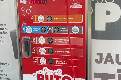 Sarkanā automazgātuves maksājumu automāta panelis ar instrukcijām.