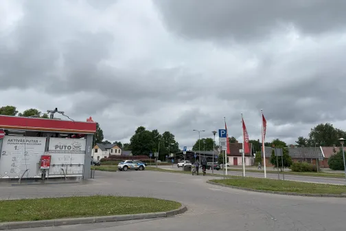 Auto mazgātuve ar pelēkām debesīm fonā, blakus iela un mājas.