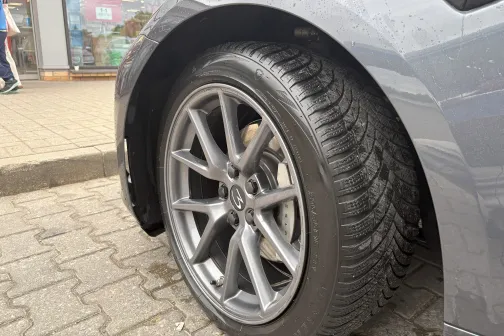 Automobiļa aizmugurējais ritenis ar melnām riepām uz bruģētas ielas.