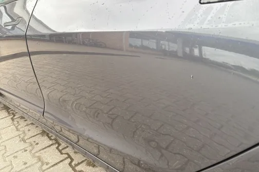 Spīdīgs automa&scaron;īnas sāns, uz kura redzama ielas atspulgs.