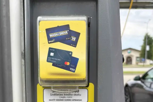 Maksājumu terminālis ar kartes attēlu, automazgātuve fonā.