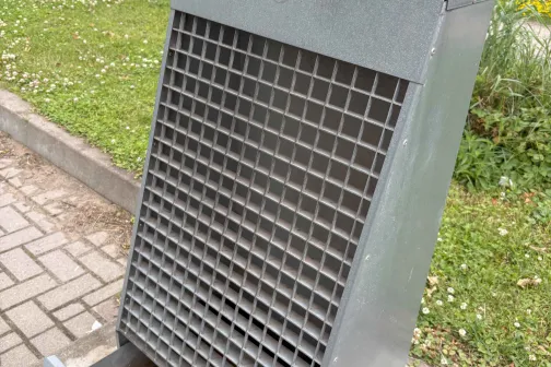 Sudraba metāla ventilācijas režģis uz trotuāra.