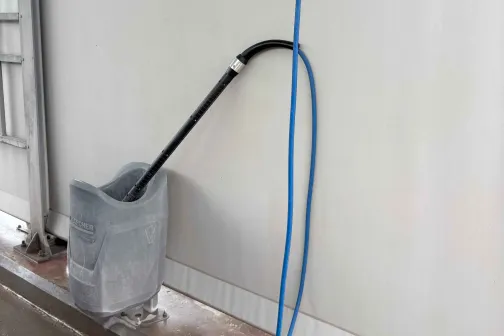 &Scaron;ļūtene un mazgā&scaron;anas aprīkojums uz grīdas pie auto mazgātavas sienas.