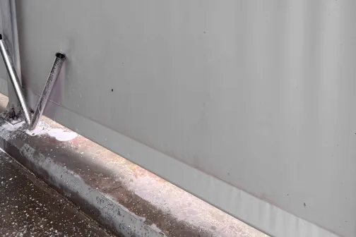 Pelēka siena ar ūdens &scaron;ļūteni pie automazgātavas.