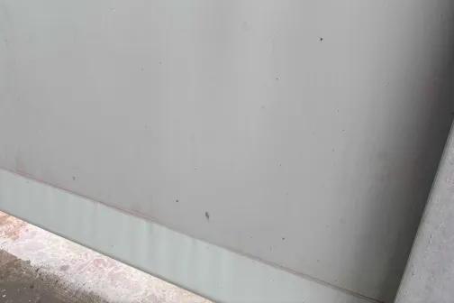 Pelēka metāla virsma ar rūsas plankumiem.