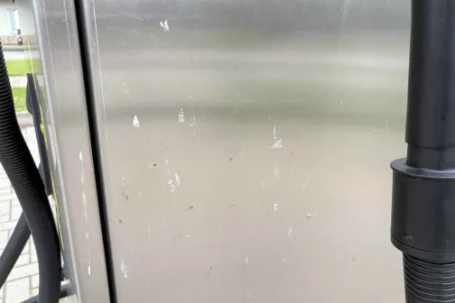 Ēnains metāla automazgātavas paneļa fragments ar trubiņu.