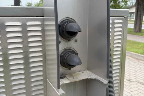 Metāla stends ar diviem melniem pogu rokturiem. Fonā koki.