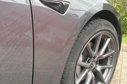 Tum&scaron;i pelēka automa&scaron;īna uz bruģēta ceļa, redzams priek&scaron;ējais ritenis.