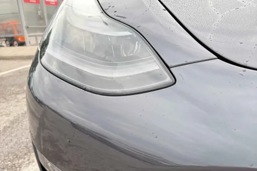 Pelēka automa&scaron;īnas priek&scaron;puse ar mitru virsmu, tuvplāns.