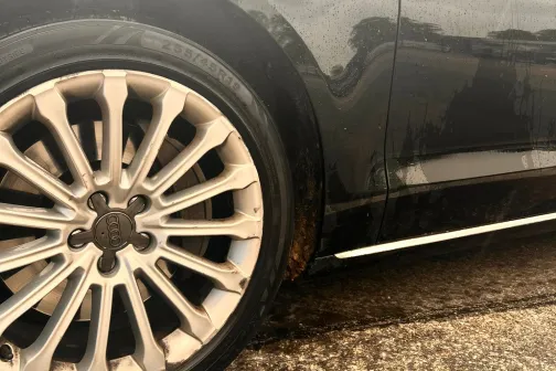 Spīdīga melna auto riteņi uz mitra asfalta.