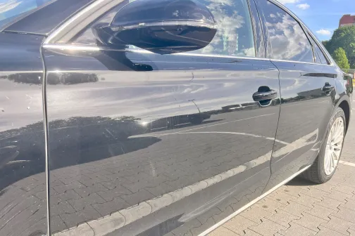 Spīdīga melna automa&scaron;īna saulē uz bruģētas autostāvvietas.