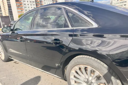 Melns auto saulainā dienā pilsētas fonā.