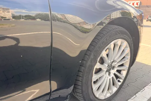 Melna automa&scaron;īna ar tīrām, spīdīgām durvīm un riepu kreisajā priek&scaron;ējā pusē.