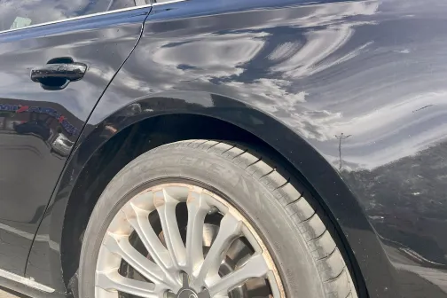 Melns auto ar netīriem riteņiem saulainā dienā.