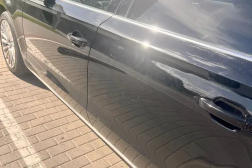 Melna automa&scaron;īna saulē, spīdīgs virsbūves klājums.