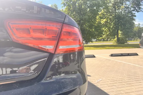 Tum&scaron;as automa&scaron;īnas aizmugure autostāvvietā, saulaina diena.