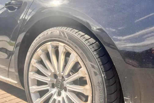 Tum&scaron;as krāsas automa&scaron;īnas spīdīgs aizmugurējais ritenis saulē.