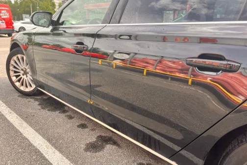 Melns automobilis ar atspulgu uz sānu durvīm stāvvietā.