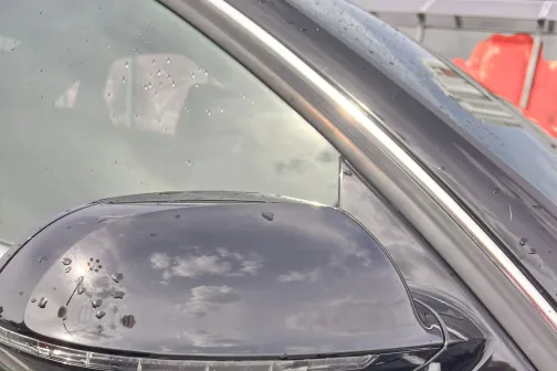 Melna automa&scaron;īna ar ūdens pilieniem uz sānu spoguļa.