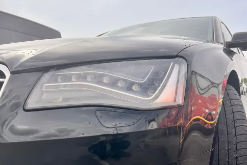 Melns auto ar tīru lukturi un mitru asfalta segumu.