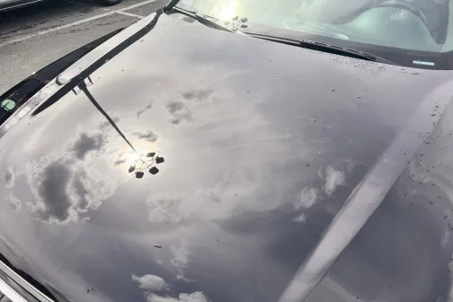 Automobiļa spīdīgs pārsegs ar atspulgu debesīs un mākoņos.