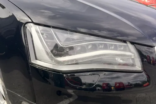 Melna automa&scaron;īna ar spīdīgu priek&scaron;ējo lukturi autostāvvietā.