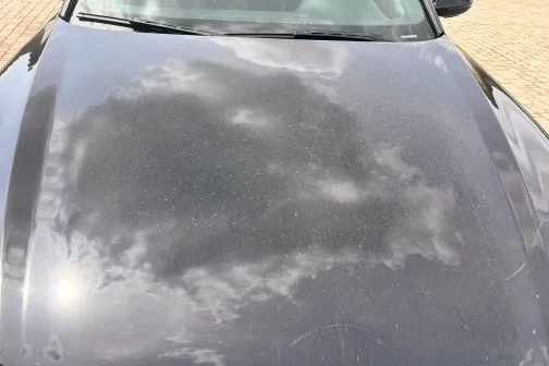 Putekļains auto pārsegs ar debesu atspulgu.