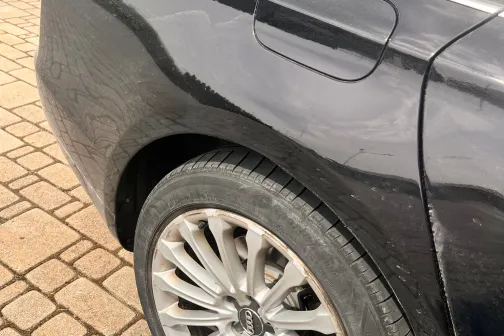 Melnas automa&scaron;īnas aizmugurējais ritenis un spārns, novietots bruģējumā.