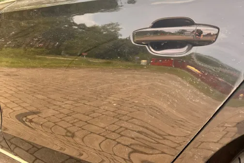 Melna automa&scaron;īna uz bruģa, atspulgs durvīs.