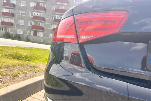 Melnas automa&scaron;īnas aizmugure pie daudzstāvu mājām saulainā dienā.