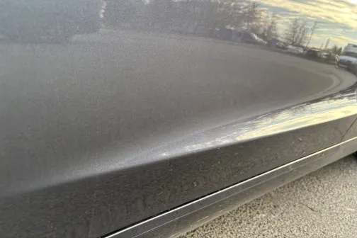 Spīdīga automa&scaron;īnas sānu virsma ar debesu atspulgu.