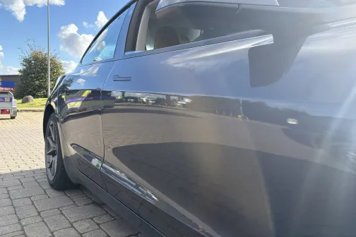 Spīdīgs melns automobilis saulainā dienā stāvlaukumā.