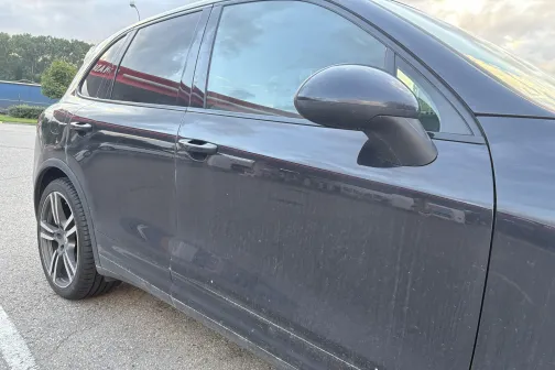 Netīrs, melns automobilis stāvvietā.